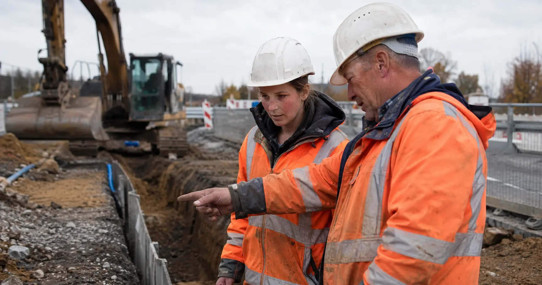 Illustrative Arbeitsszene mit zwei Beschäftigten auf einer Tiefbaustelle